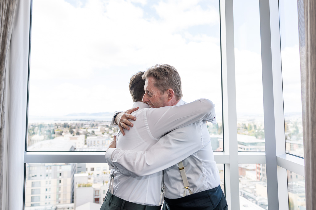 groom and dad hugging near a hotel window with beautiful view