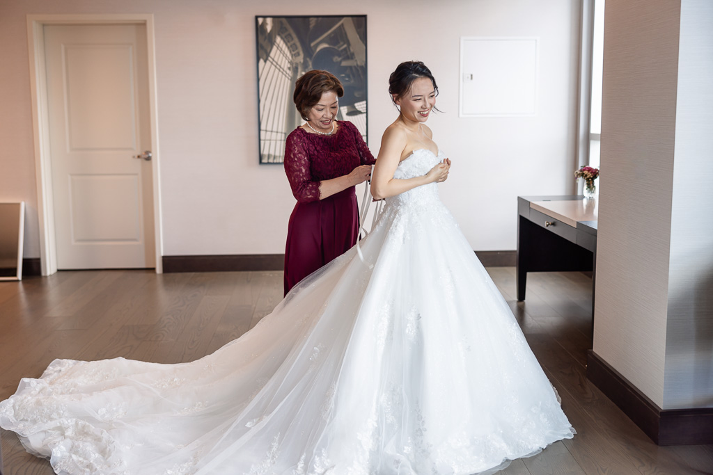 Mom helping bride with dress in hotel room