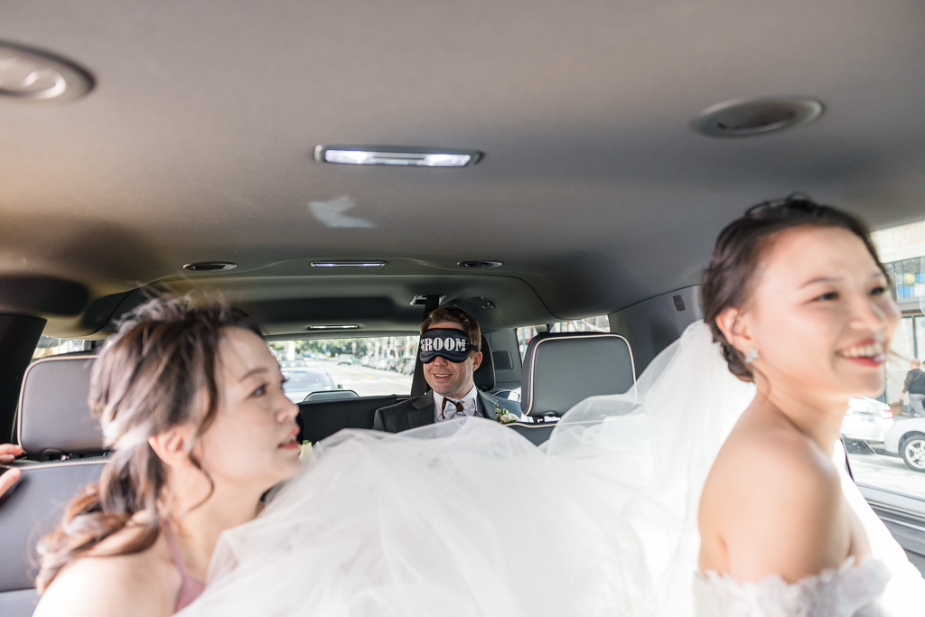 bride in the front seat and groom in the back wearing a blindfold