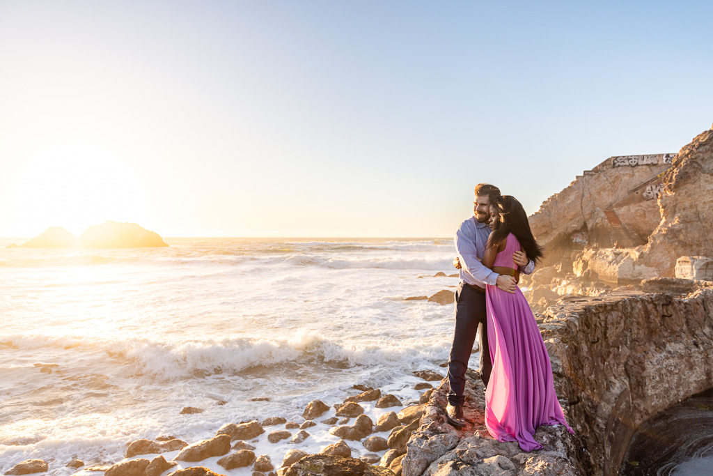 stunning ocean sunset engagement photos in purple dress with waves crashing onto rocks