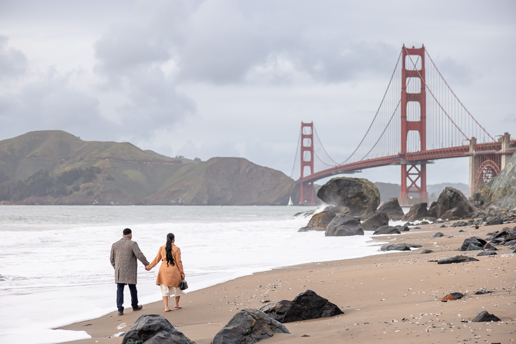 couple walking along the beach towards the Golden Gate Bridge