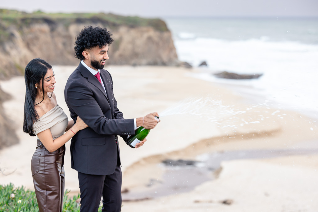 popping a bottle of champagne over a beach cliff