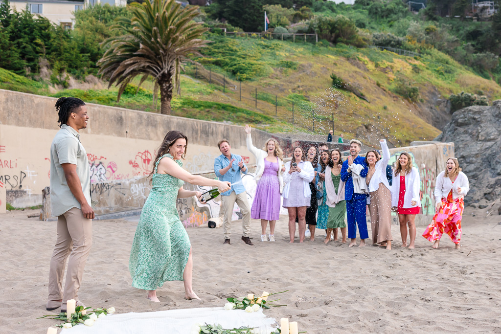 popping champagne with colorfully-dressed friends behind them