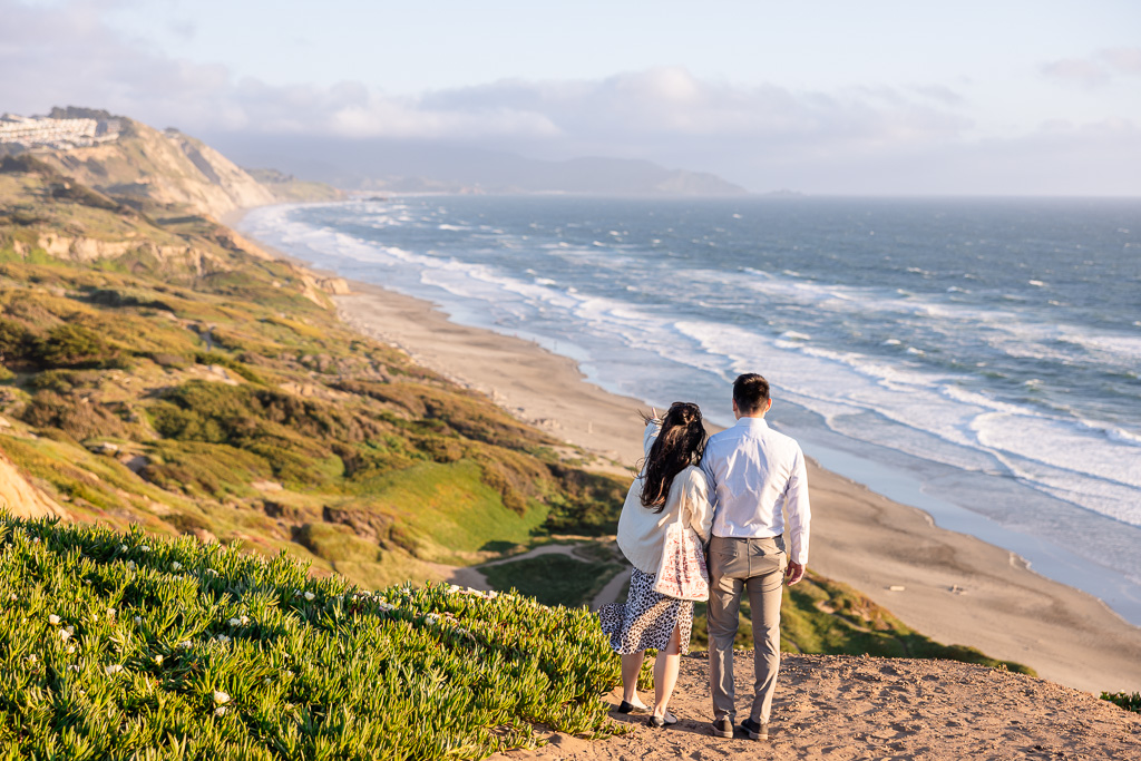 couple standing on ocean bluff looking out towards the waves