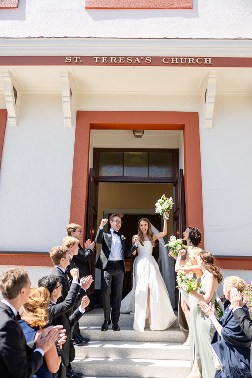 bride and groom cheering as they exit St Teresa of Avila Catholic Church with bridal party receiving them