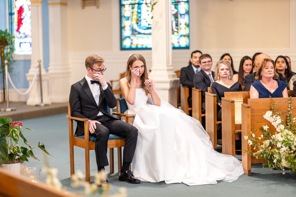 bride and groom wiping away tears during church ceremony