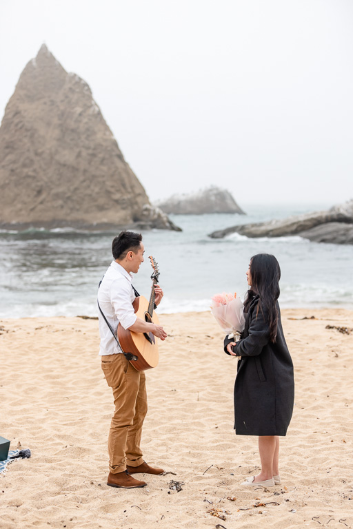 man playing guitar to his girlfriend on the beach