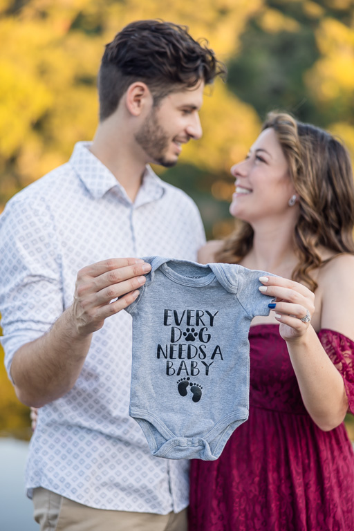 Expecting couple holding a gray baby onesie that says, 