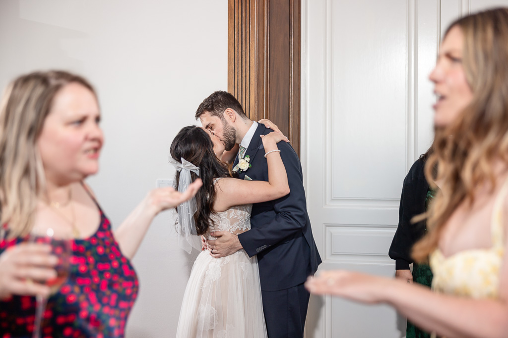 a funny candid photo of the bride and groom kissing behind some guests