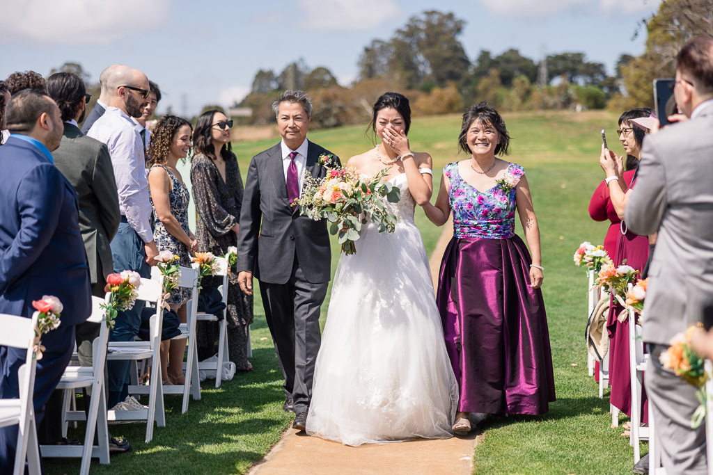 bride covering up a tear as she walks down the aisle to her groom