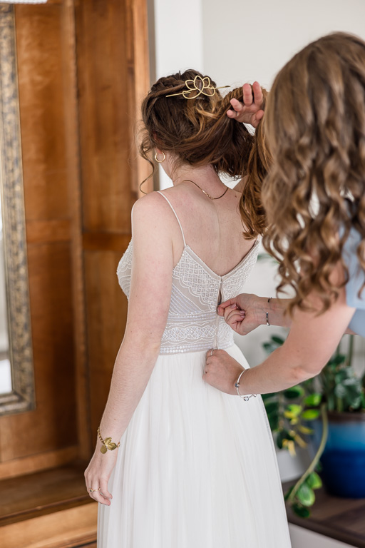 zipping up back of bride’s dress