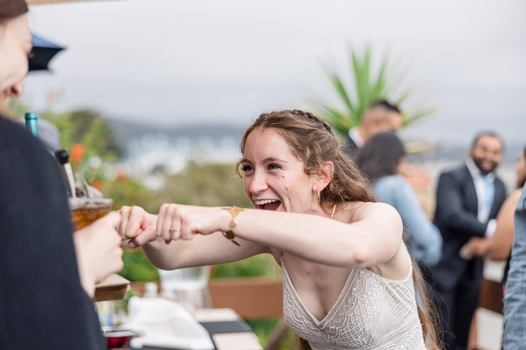 bride thoroughly enjoying herself at cocktail hour by fist bumping friends