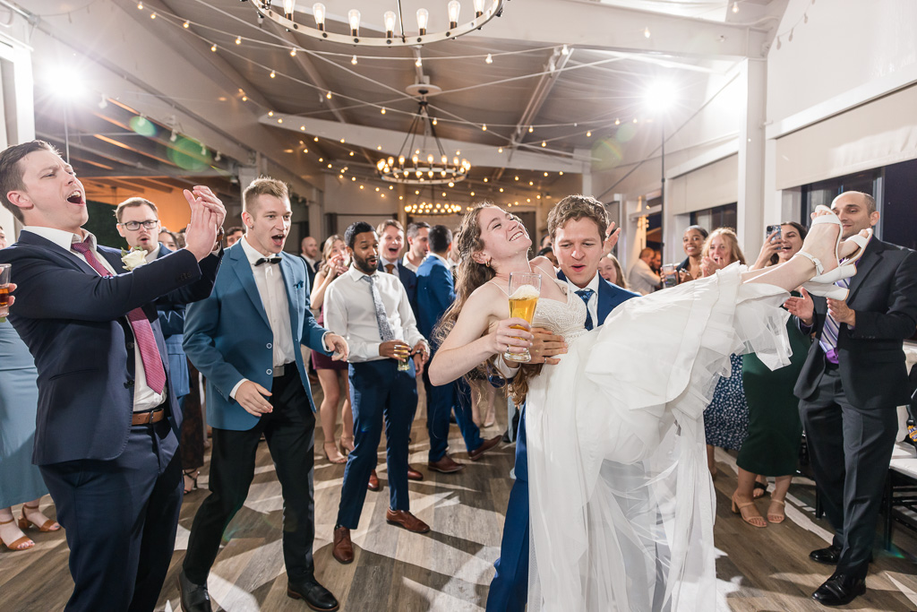 groom swinging the bride around on the dance floor as she holds a glass of beer