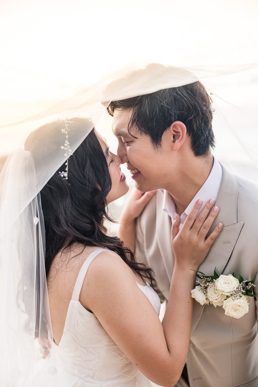 close-up photo of bride and groom under veil at sunset