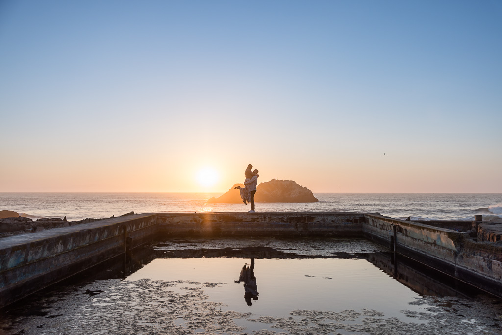 lifting up engagement photo of couple at Sutro Baths with reflection