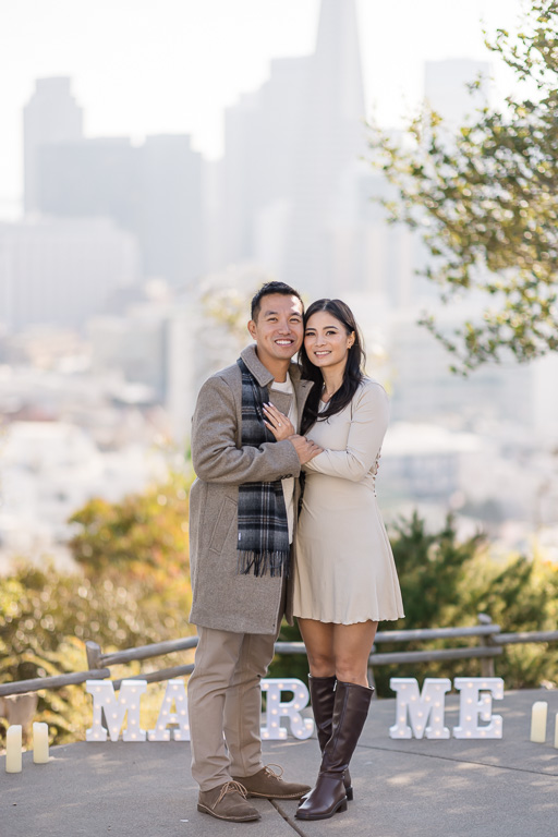 a photo of the newly engaged couple standing in front of marry me letters