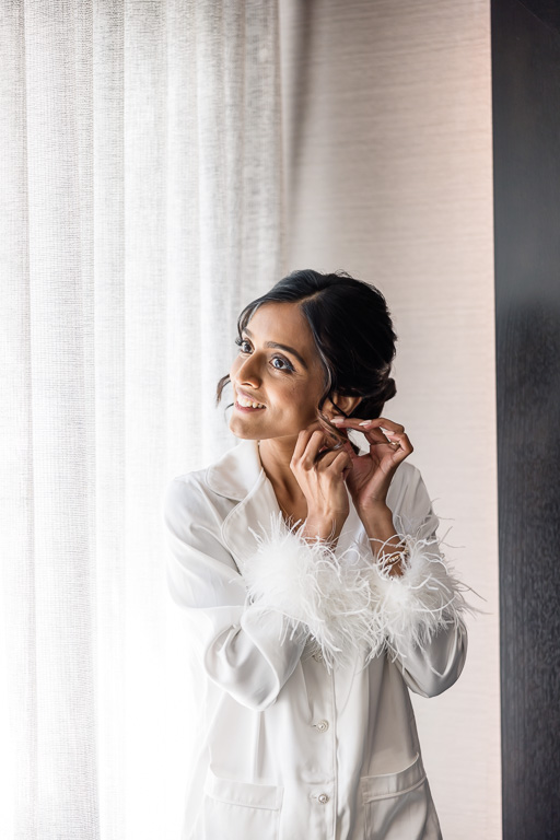 bride putting on earrings in hotel room