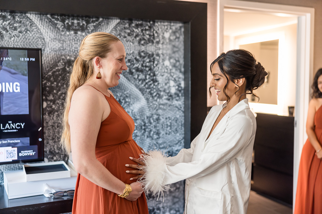 bride admiring her friend and bridesmaid's baby belly