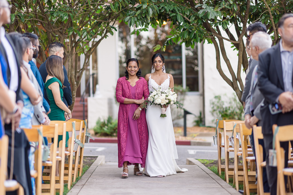 bride walking down the aisle while accompanied by her mother