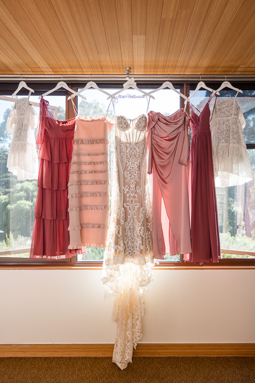 bride and colorful bridesmaid dresses hanging up against a window