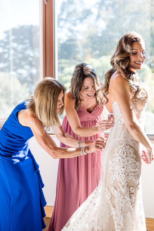 bridesmaids helping bride button up her dress