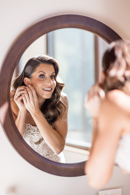 bride putting on her earrings in a mirror