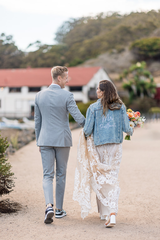 Candid photo of bride and groom walking away wearing a Mrs denim jacket