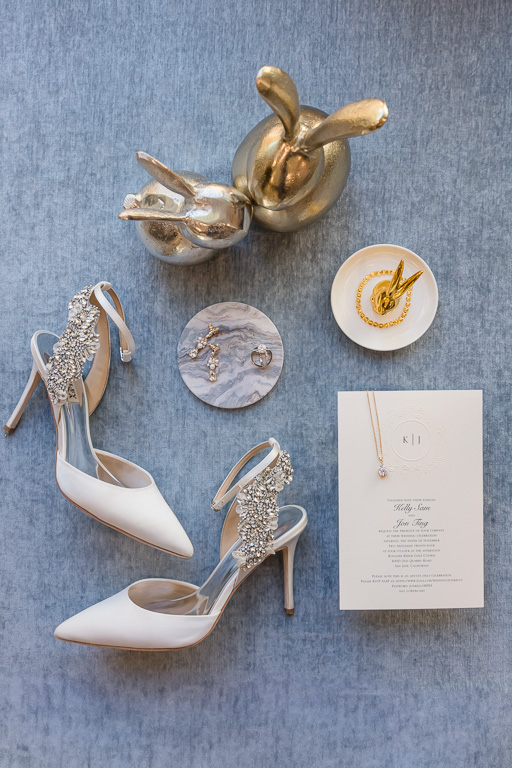 wedding flat lay on gray background with invitations, necklace, rings, earrings, shoes