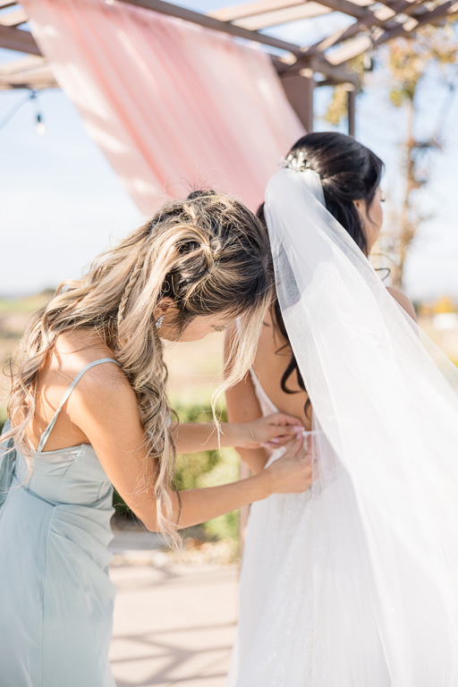 bridesmaid helping bride button up her dress