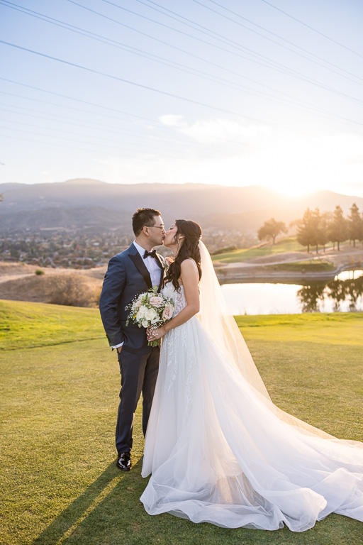 kissing photo of bride and groom as sun sets behind mountains in the distance