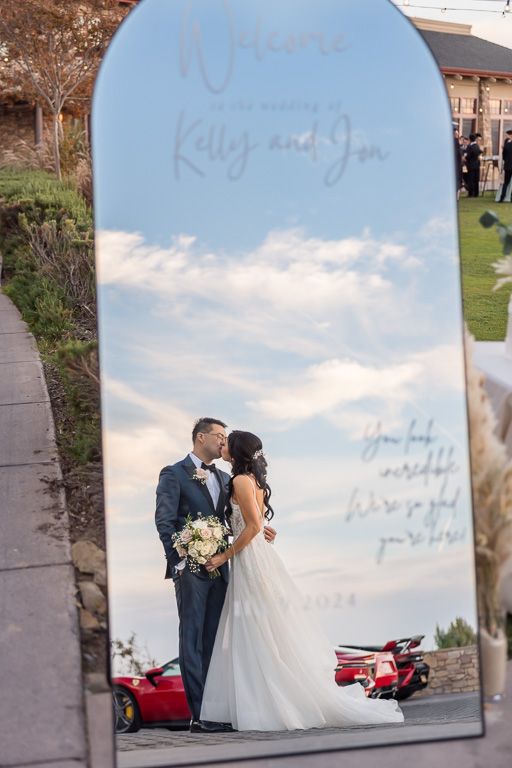 bride and groom kissing in a mirror with red cars behind them