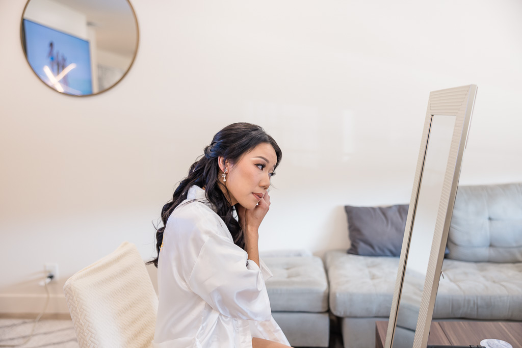 bride putting on her earrings in front of a mirror