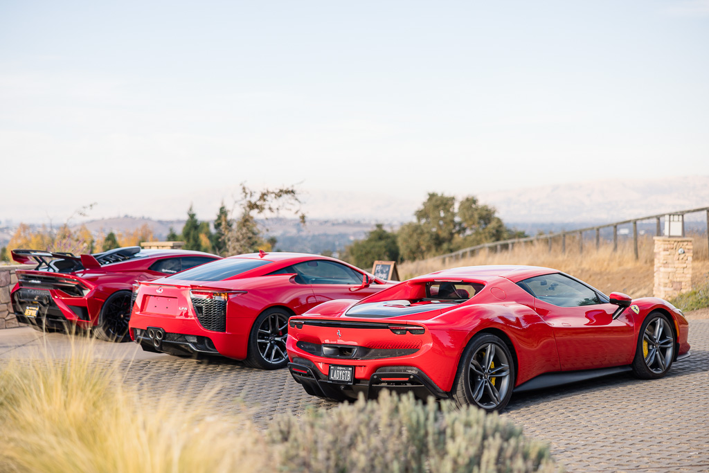 Lamborghini, Lexus LFA, and Ferrari cars parked on a hilltop at the entrance of a wedding