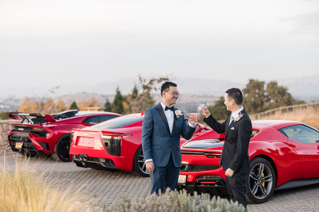 groom and best man having a drink next to three fancy exotic red sports cars