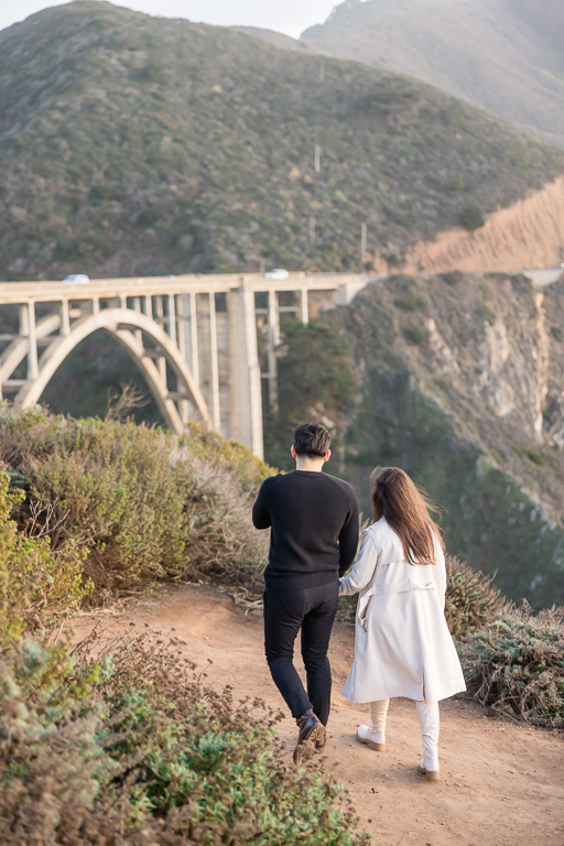 couple walking towards the Bixby Bridge along the cliffside