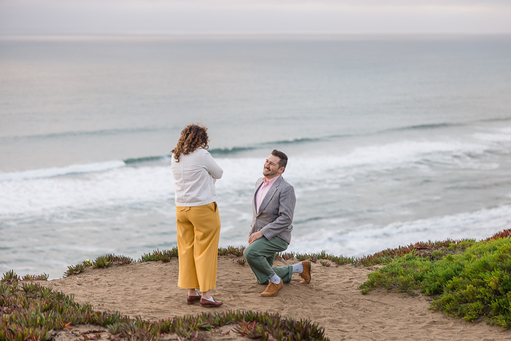 kneeling down to propose on a patch of sand