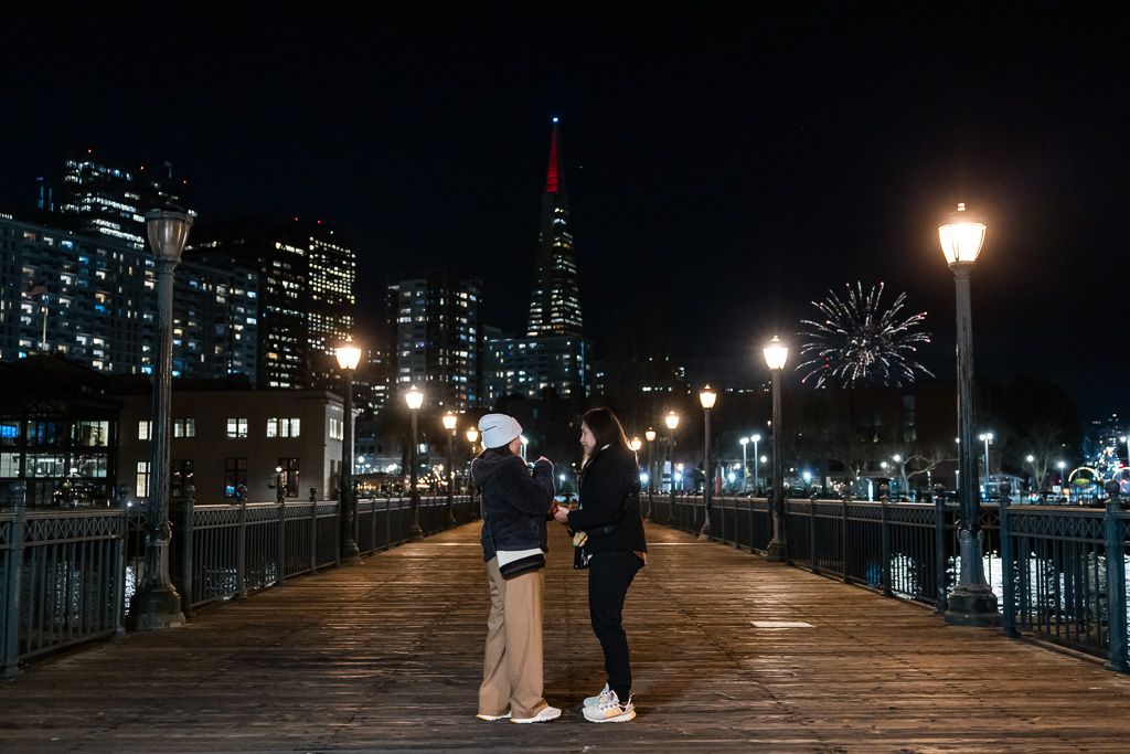 couple about to propose in front of the downtown skyline at night with fireworks going off