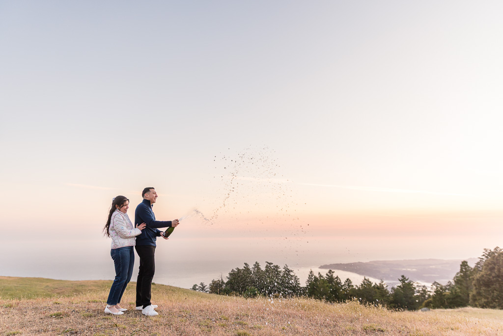 spraying champagne to celebrate engagement at sunset on a mountaintop