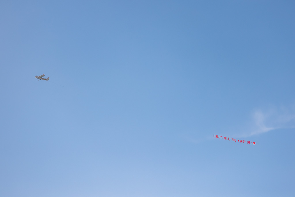 airplane towing a banner with a marriage proposal written on it