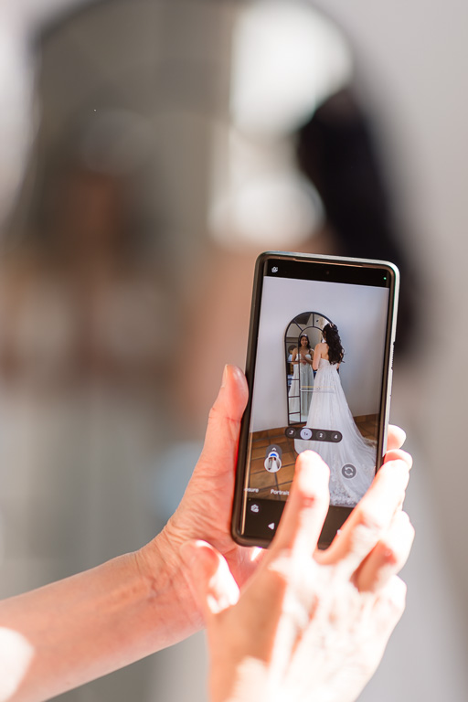 mom taking a phone photo of bride in front of a mirror