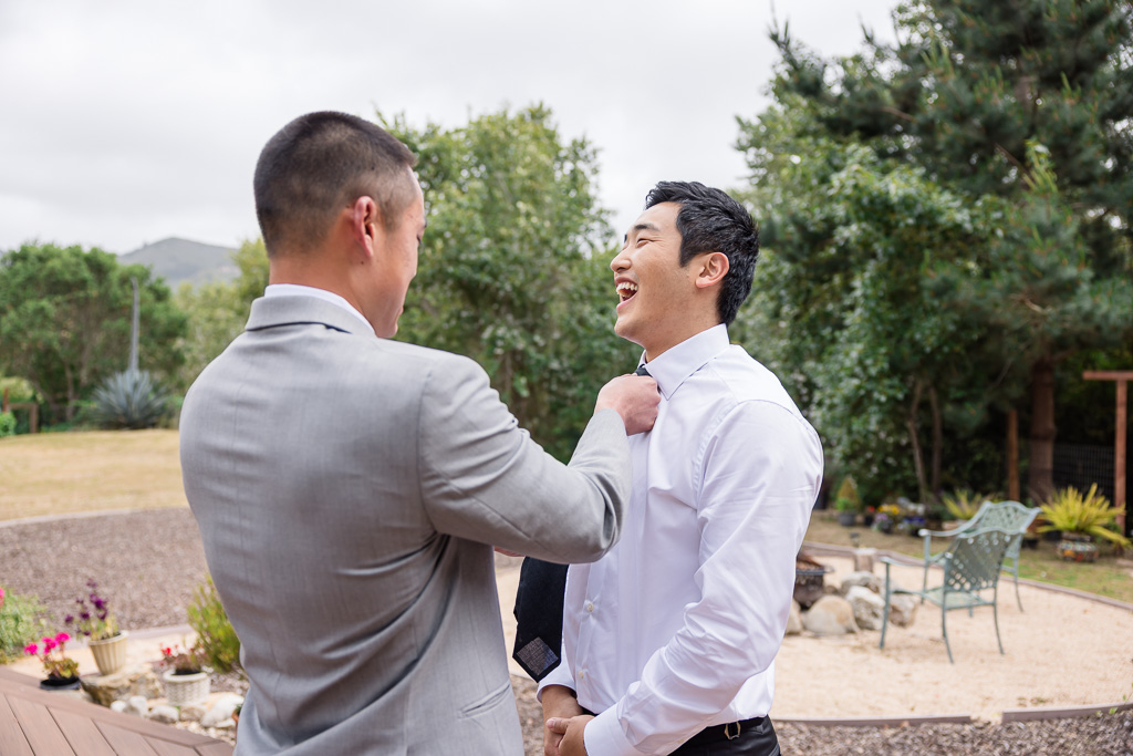 groomsman helping groom put on his tie