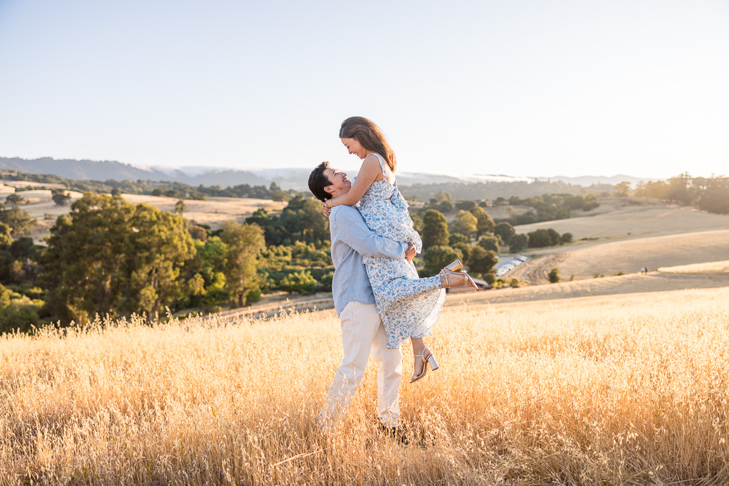 engagement photos lift-up pose on golden grassy field at sunset