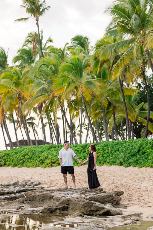 Engaged couple strolling along a path lined with towering palm trees in Oahu’s Ko Olina resort, capturing tropical Hawaii vibes.