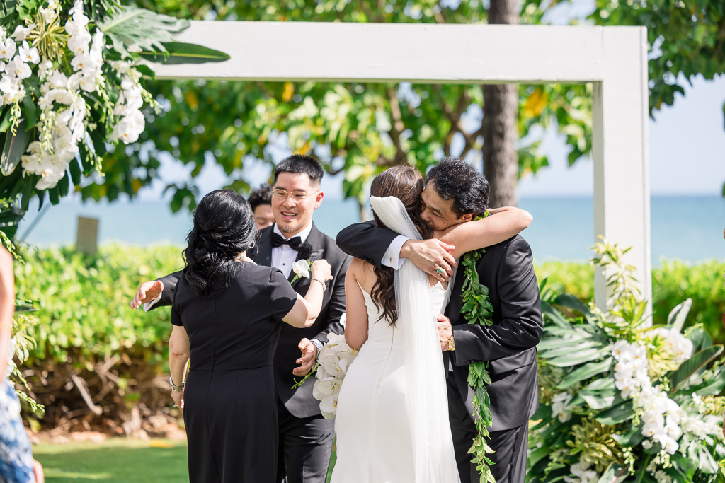 bride's parents hugging the bride and groom as she is received at the end of the aisle