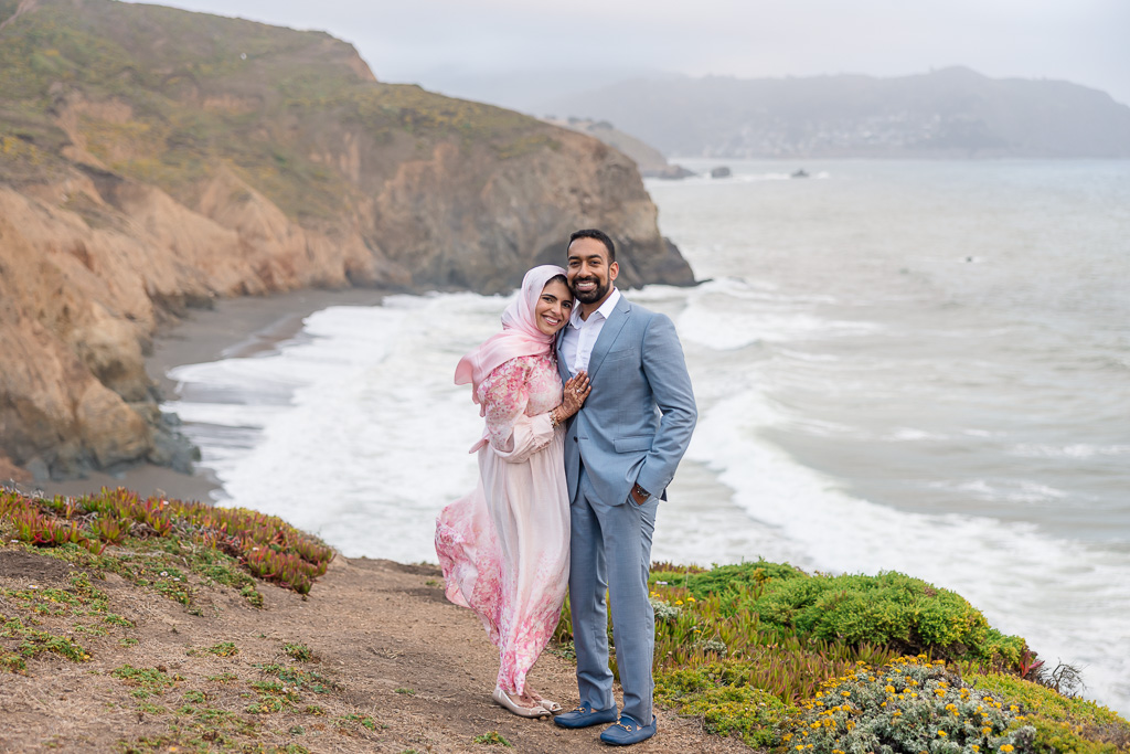 couple standing atop cliff by the ocean