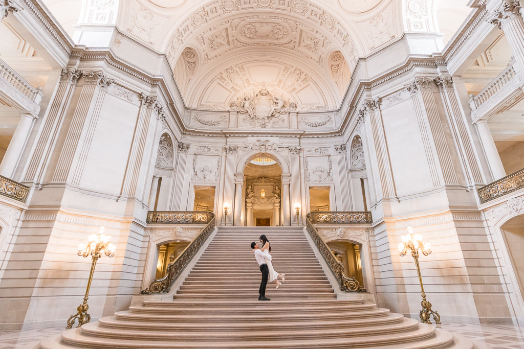 classic SF City Hall grand staircase wedding photo of groom lifting up the bride