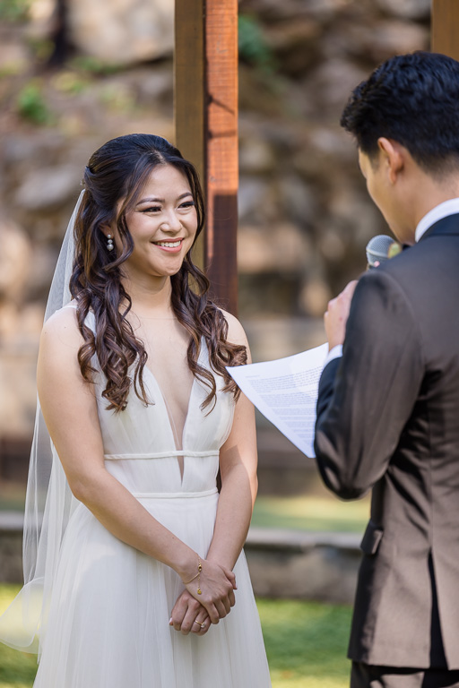 bride smiling sweetly at the groom while he gives his personal written vows