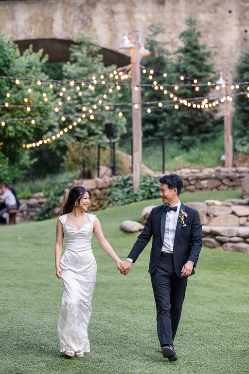 wedding portrait of the couple walking on a grassy lawn with string light accents behind them