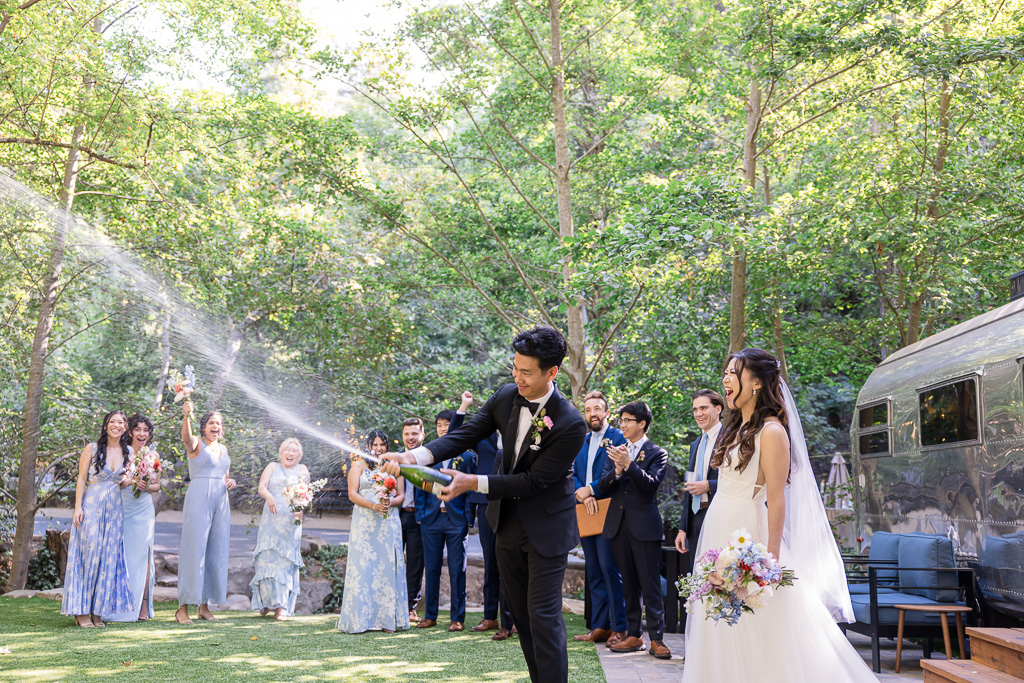 groom spraying champagne with the bride next to an Airstream trailer