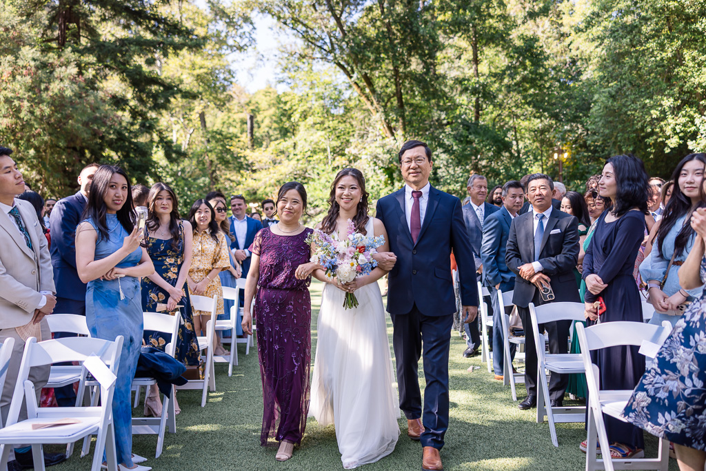 bride being escorted by both of her parents in the aisle